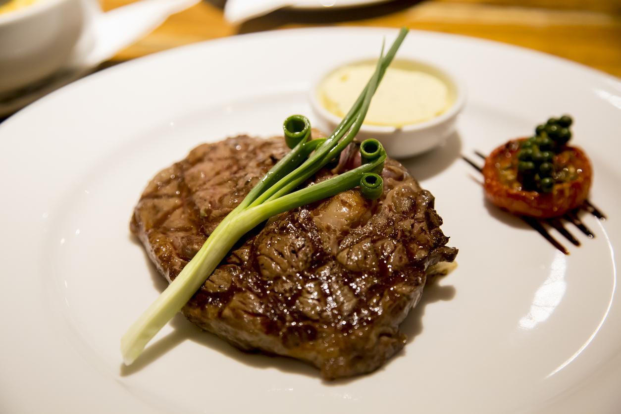 Grilled steak with green onions, a side of sauce, and a grilled tomato on a white plate